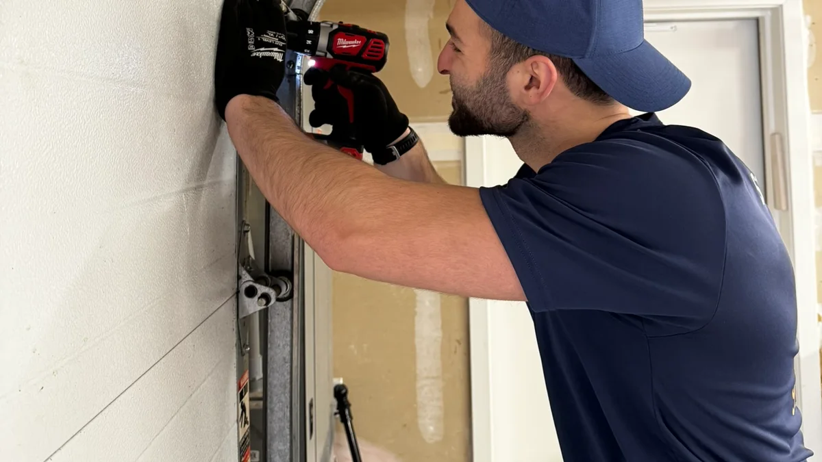 Technician inspecting hardware beside a white sectional garage door