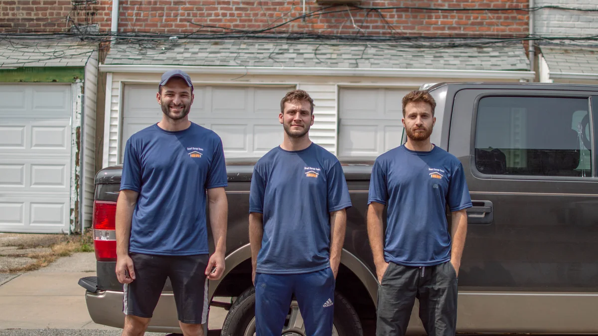 Three garage door technicians standing beside a service van
