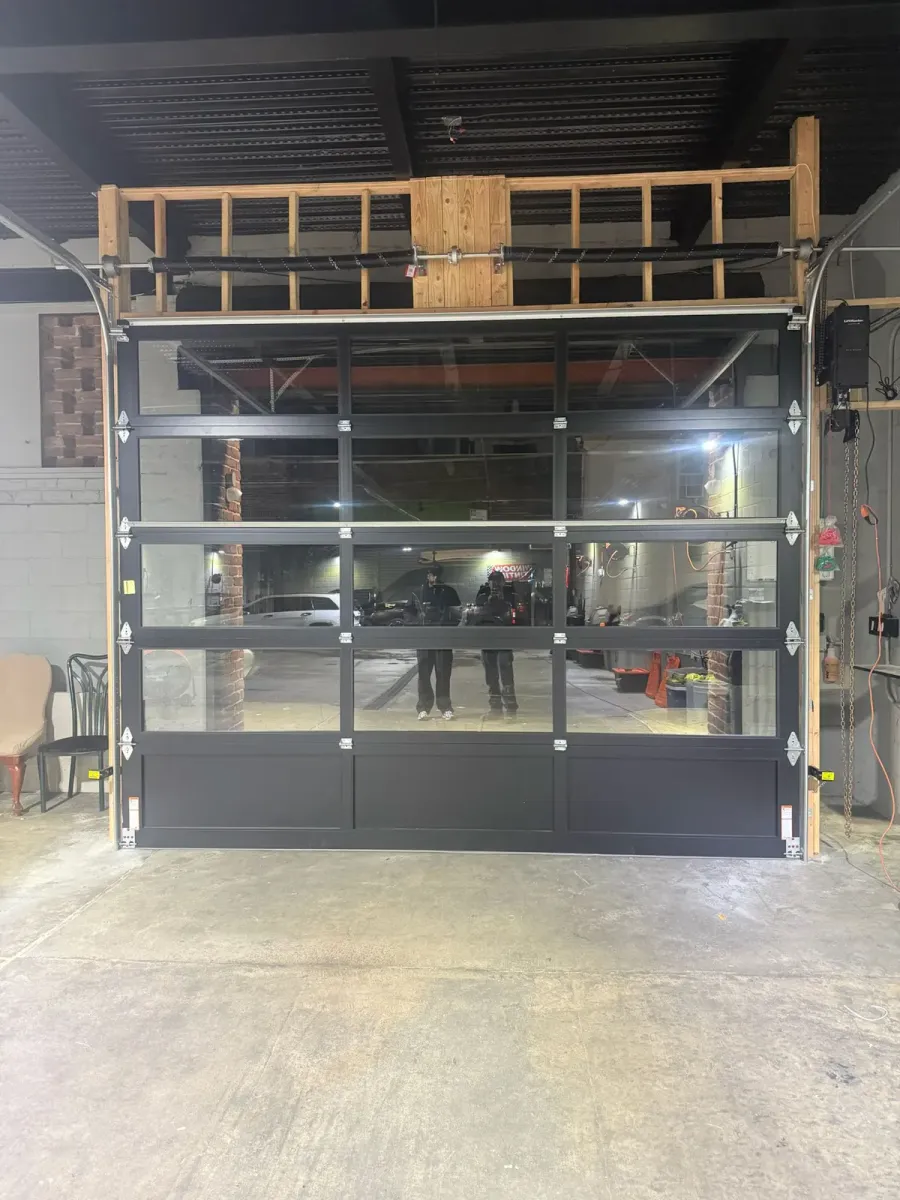 Full-view garage door with a black aluminum frame and glass panels, torsion springs above and a wall-mounted opener — installed by Smart Garage Doors