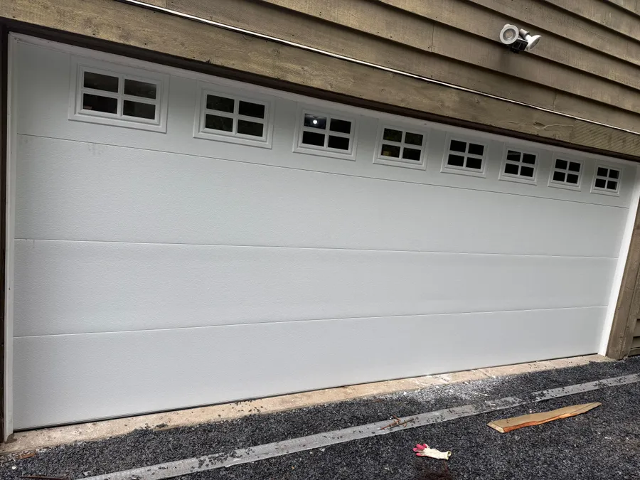 Wide double garage door with two rows of divided-light window inserts, freshly installed on Long Island, NY